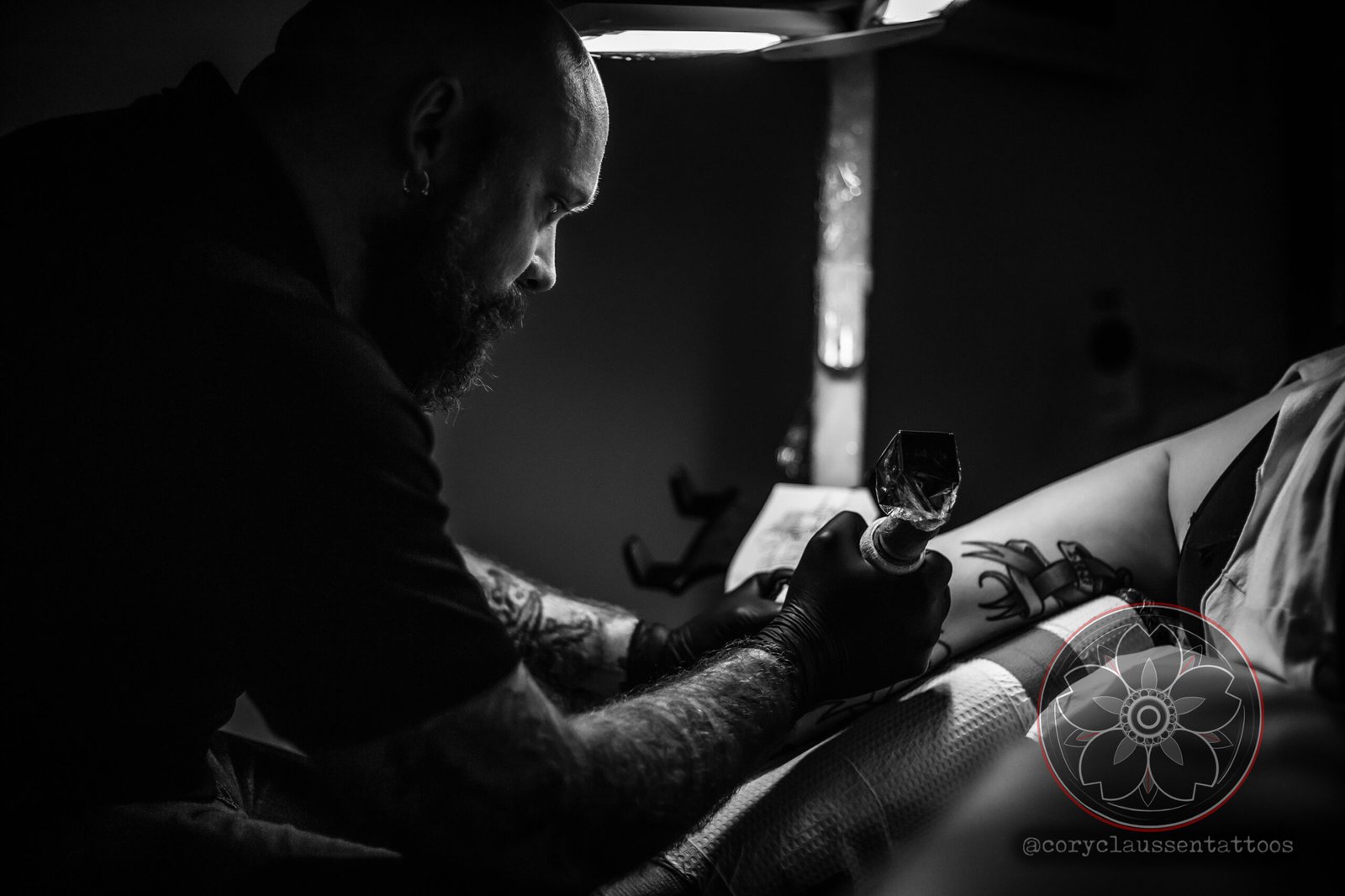 Cory Claussen, head of Red Arbor Tattoo, focused on tattooing a client’s arm in a dimly lit studio.