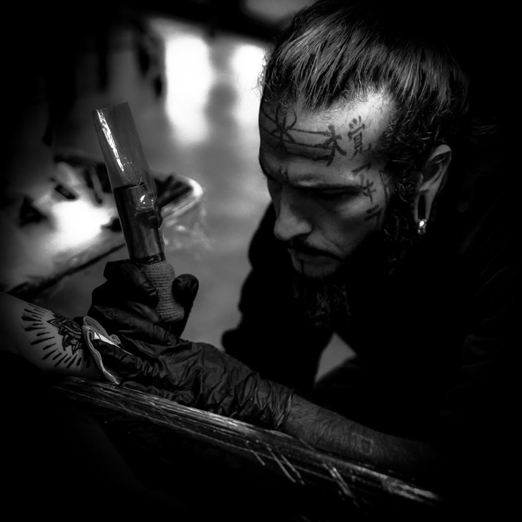 Johnny Threewolves, a tattoo artist at Red Arbor Tattoo, focused intently while tattooing intricate linework on a client’s arm.