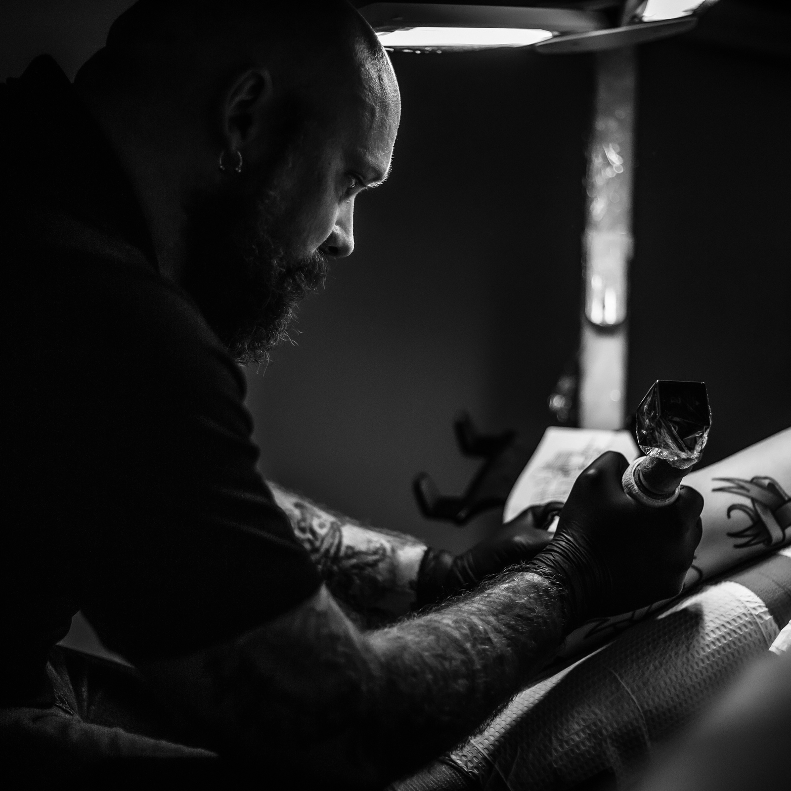 Cory Claussen, head of Red Arbor Tattoo, focused on tattooing a client’s arm in a dimly lit studio.