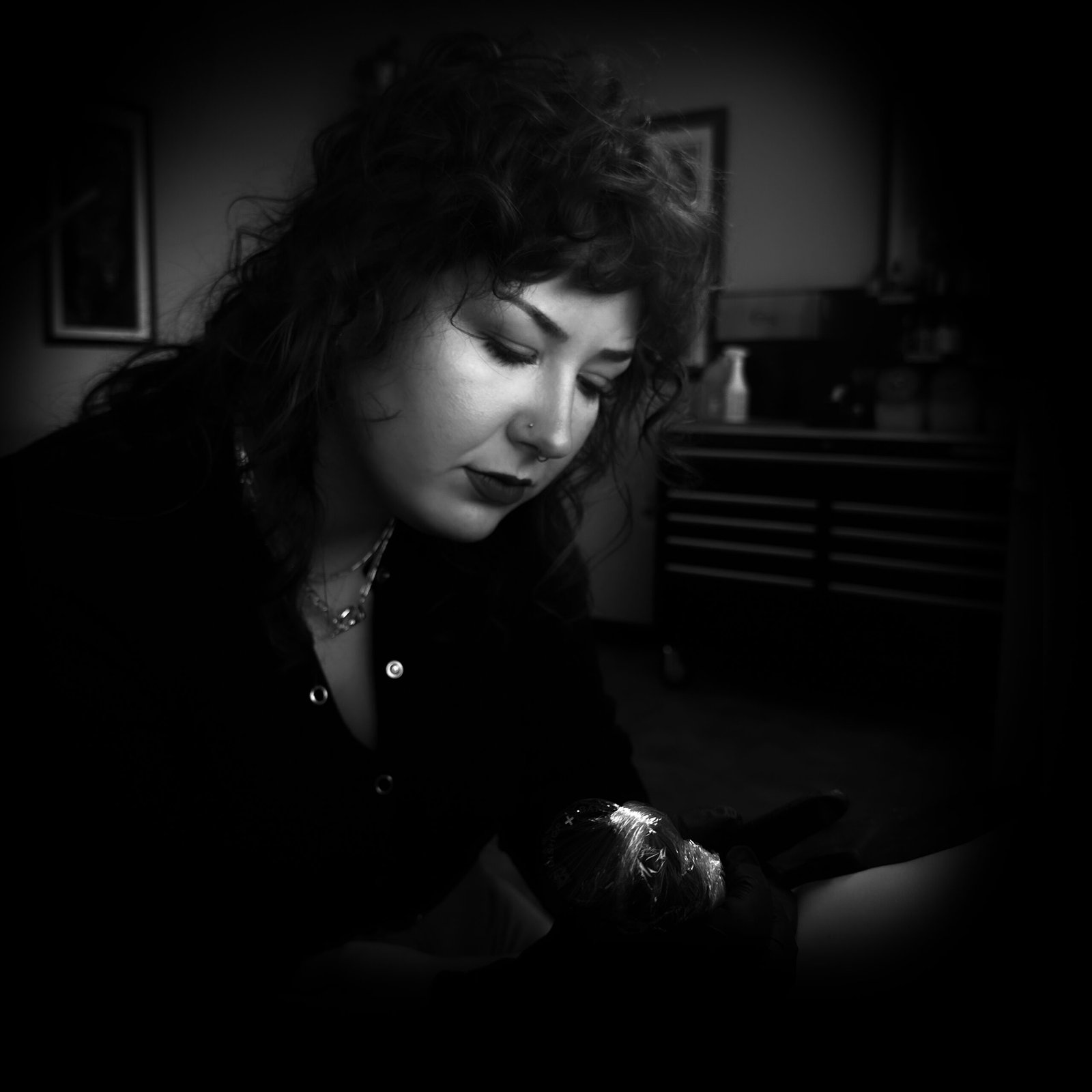 Libby Murphy tattooing a client with focused attention, captured in a black-and-white photograph under soft studio lighting.